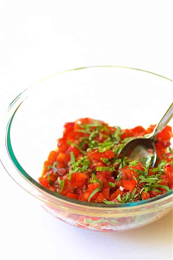 Photo of tomato salsa and fresh basil being stirred in glass mixing bowl.