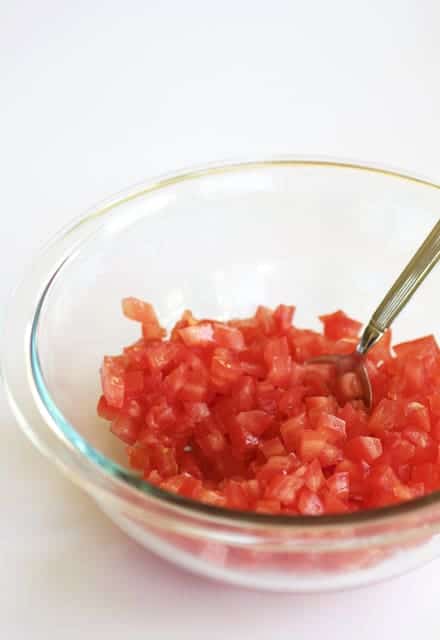 Photo of diced tomatoes in glass mixing bowl being stirred with spoon.