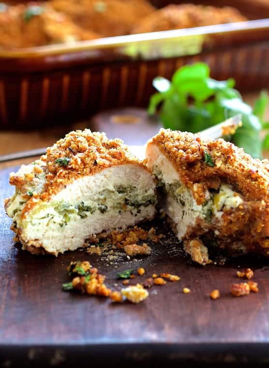 Photo of one Green Chile Goat Cheese Stuffed Chicken Breasts with Spicy Pecan Cornmeal Crust cut in half on wood cutting board.