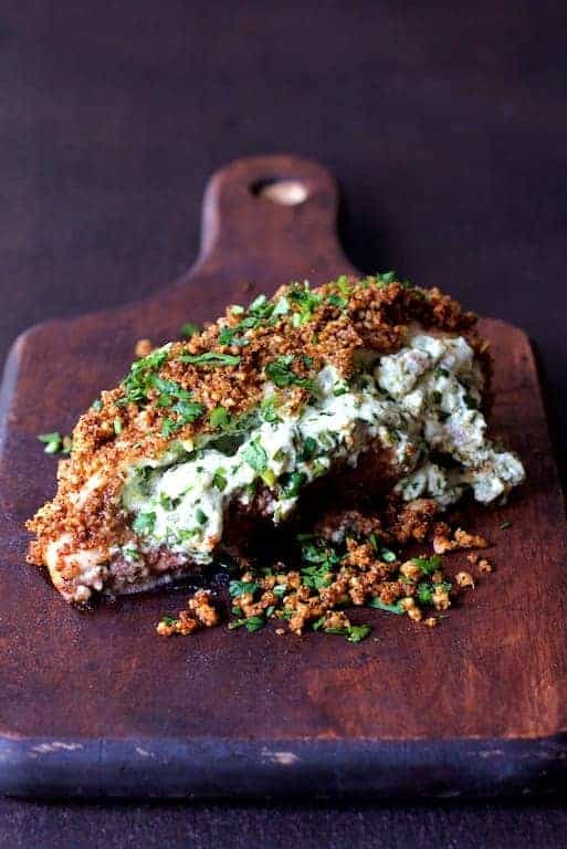 Green Chile Goat Cheese Stuffed Chicken Breasts with Spicy Cornmeal Pecan Crust on wood cutting board.