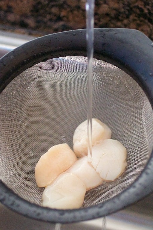 Photo of scallops being rinsed with running water in a sieve.