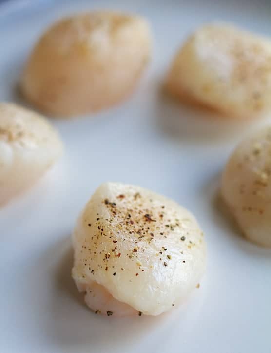 Photo of uncooked scallops seasoned with salt and black pepper.