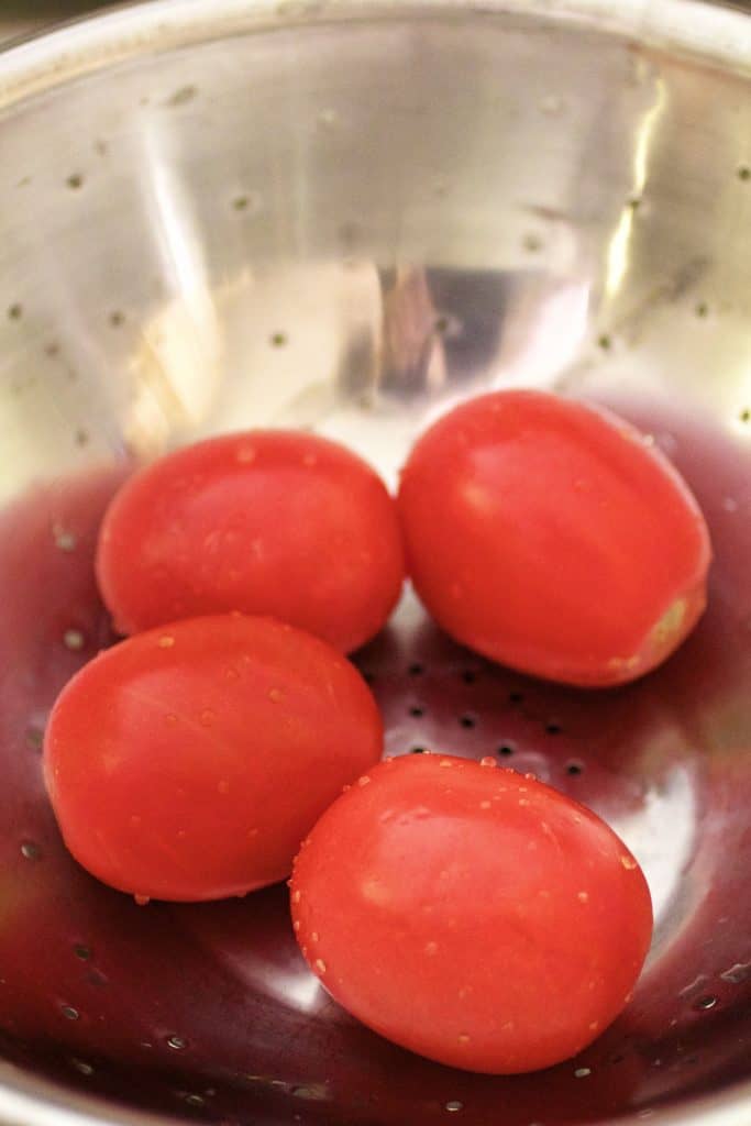 Photo of four tomatoes in stainless steel colander.