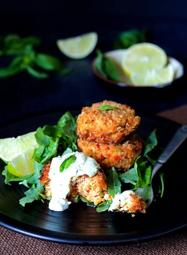 Photo of Thai Salmon Cakes with Basil - Lime Mayonnaise on black plate garnished with lime wedges and arugula.