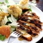 Sliced Blackened Chicken Caesar Salad on white plate with fork digging into one of the slices.