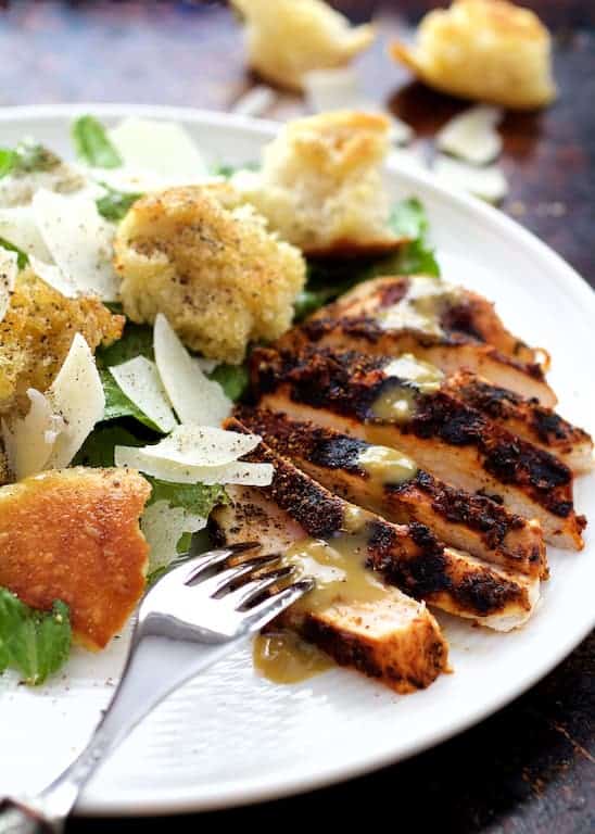 Sliced Blackened Chicken Caesar Salad on white plate with fork digging into one of the slices.