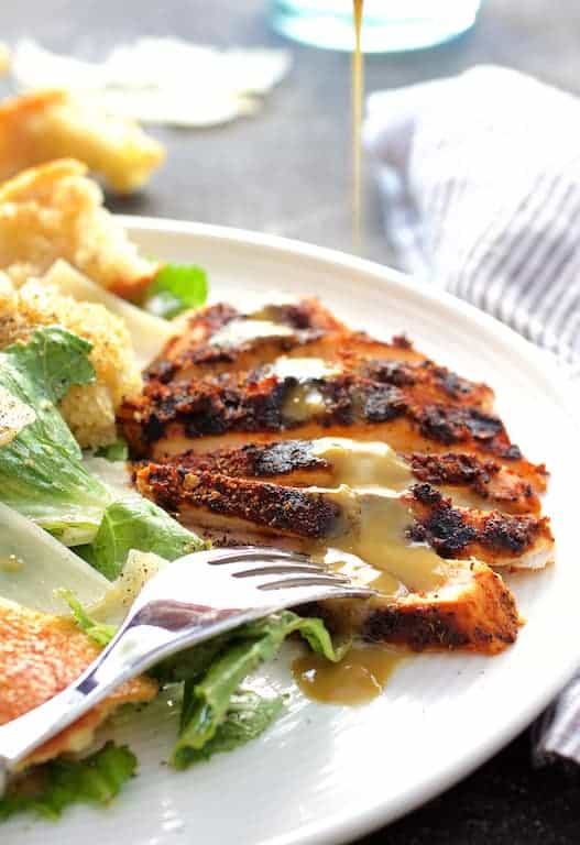 Photo of Blackened Chicken Caesar Salad with Sourdough Croutons with dressing being drizzled over chicken.