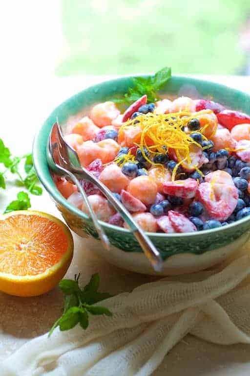 Summer Fruit Salad with Orange Yogurt Vanilla Dressing in green decorative bowl garnished with orange zest.
