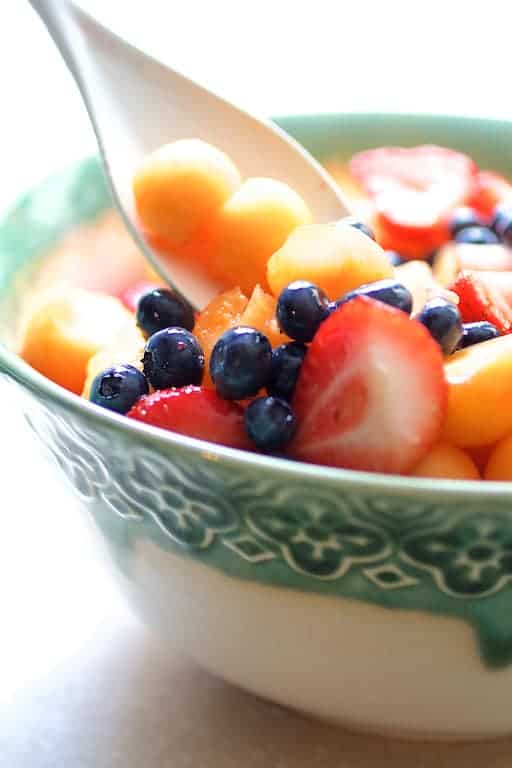 Photo of fruit salad being stirred with white spoon.