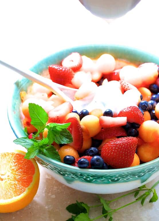Photo of Orange Yogurt Vanilla Dressing being poured over fruit salad.