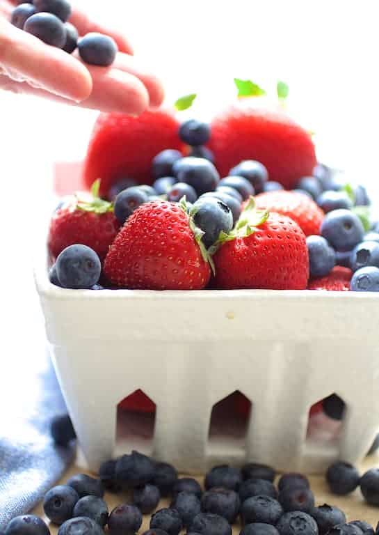 Photo of fresh blueberries and strawberries in white fruit basket.