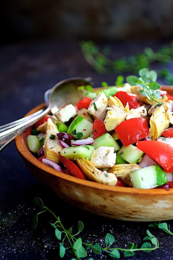 Photo of Greek Vegetable Salad with Marinated Feta Cheese in wood bowl on dark blue background/