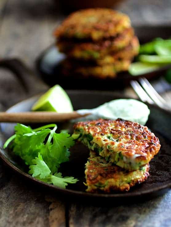 Photo of a Whole Grain Zucchini Jalapeno Fritter cut in half on cast iron pan with spoonful of sour cream in the background.