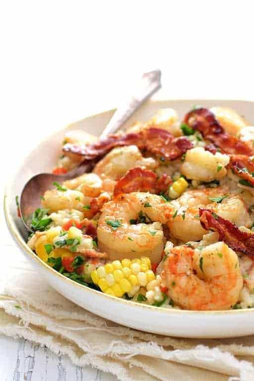 Shrimp and Corn Risotto with Bacon in white bowl with serving spoon.