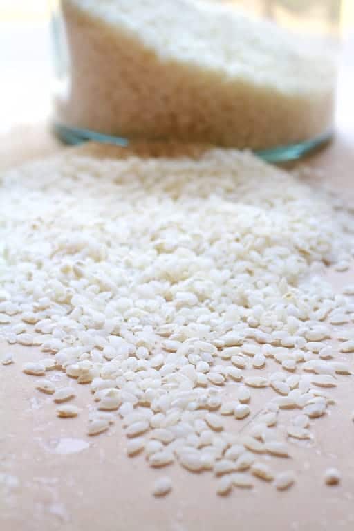 Photo of arborio rice spilled out onto marble surface with jar in the background.