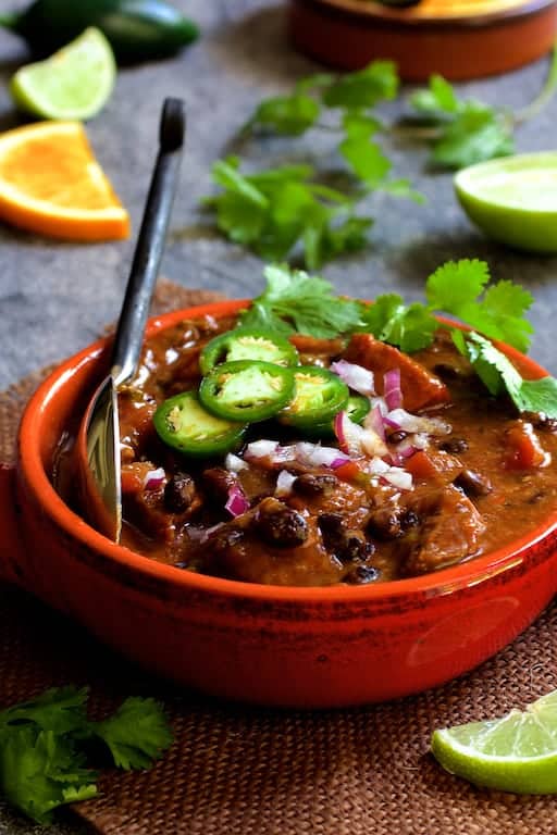 Photo of Feijoada (Brazilian Beef Stew) in red clay bowl garnished with jalapeno slices, cilantro and fruit wedges.