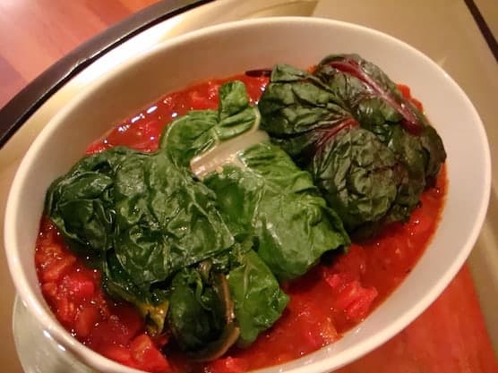 Photo of stuffed Swiss chard rolls on tomato sauce.
