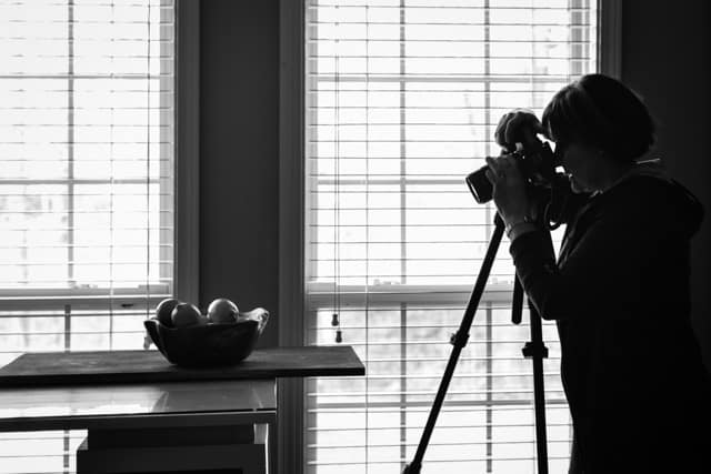 Photo of Carol Borchardt taking a food photo in front of window.