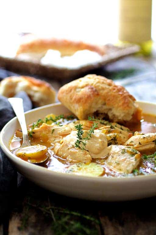 Photo of Chicken Bouillabaisse in white bowl with bread resting on the bowl.