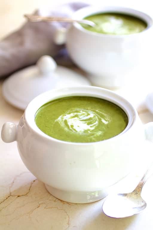 Photo of Cream of Green Vegetable Soup in white bowl on marble surface with cream swirled in.