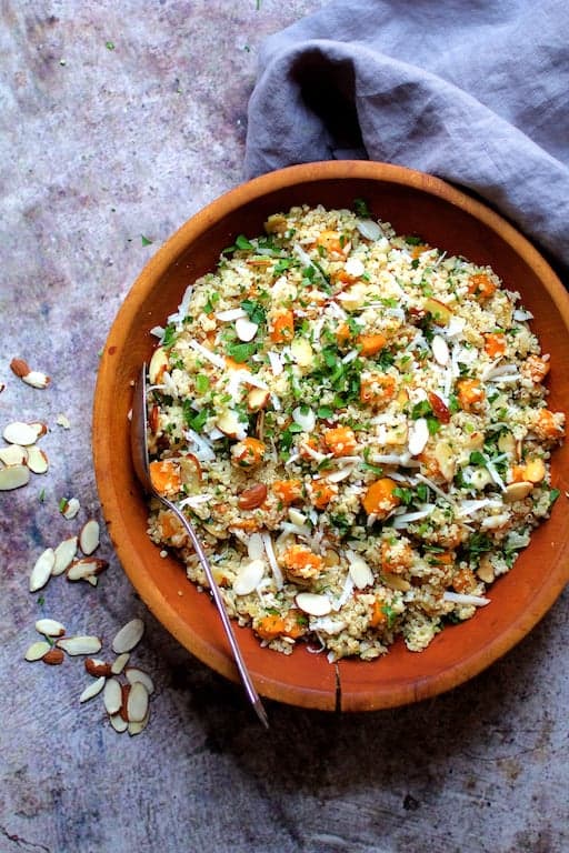 Photo of Lemony Quinoa with Butternut Squash, Almonds and Parmesan Cheese in wooden bowl with serving spoon on gray background with gray napkin.
