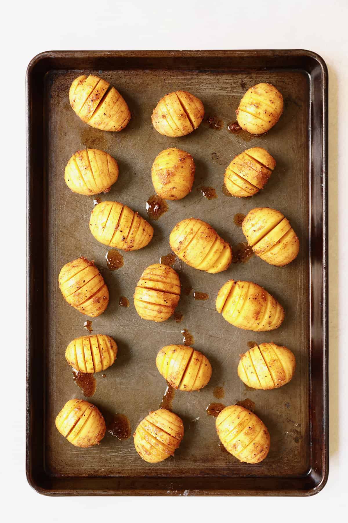 Photo of seasoned hasselbacked potatoes on baking sheet before baking.