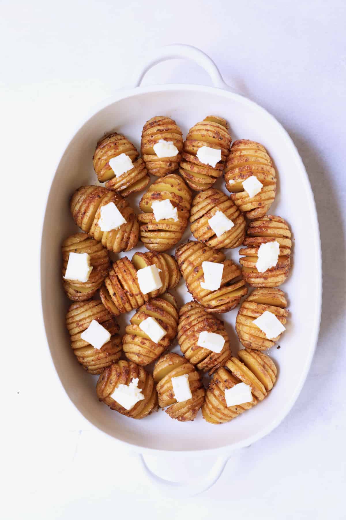 Photo of roasted hasselbacked potatoes in white baking dish dotted with butter.