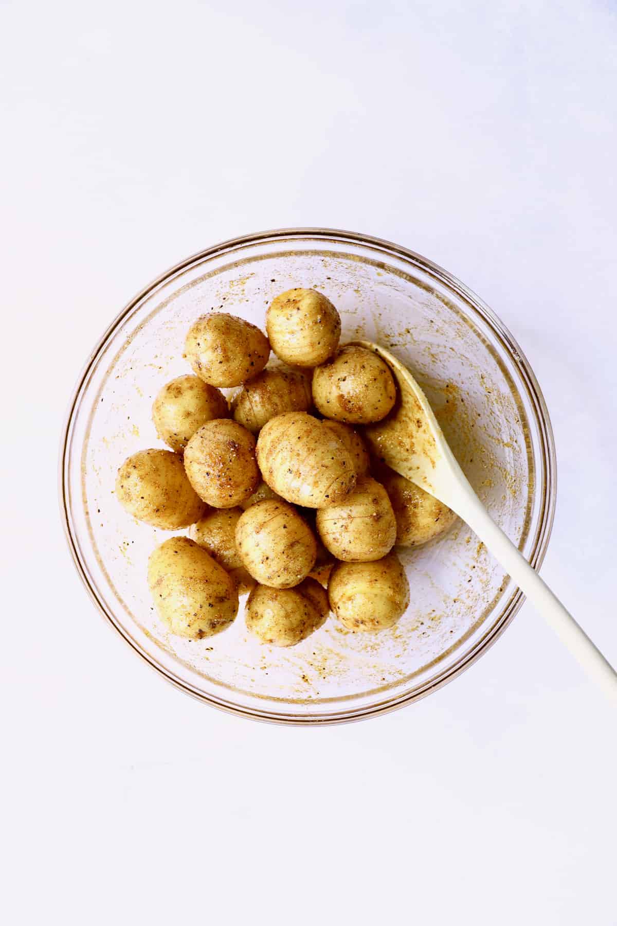 Photo of Yukon gold potatoes in glass bowl being tossed with oil and spices.