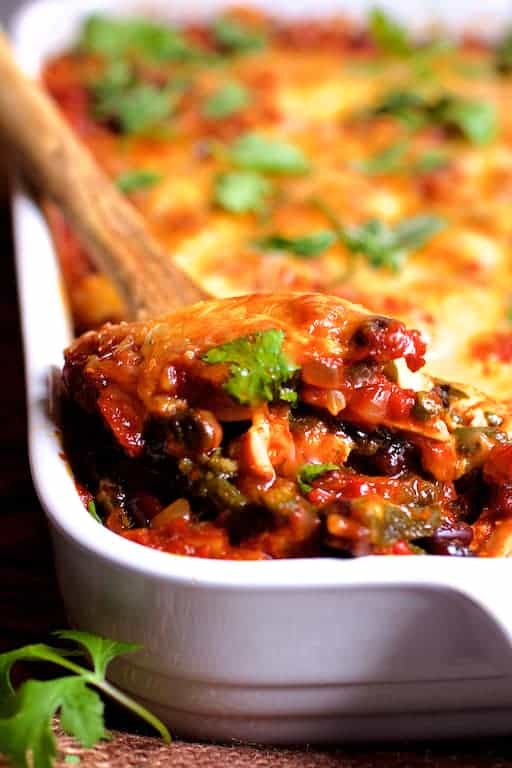 Close-up photo of a spoonful of Chicken Poblano and Black Bean Tortilla Casserole being scooped out of baking dish.