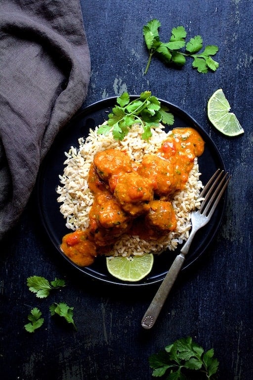 Photo of Meatballs in Spicy Curry over rice on black plate.