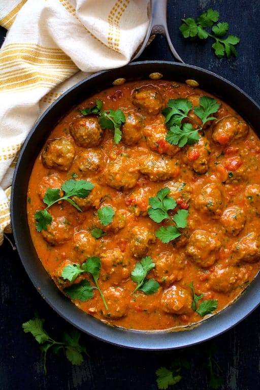 Photo of Meatballs in Spicy Curry smothered in sauce in skillet garnished with cilantro sprigs.