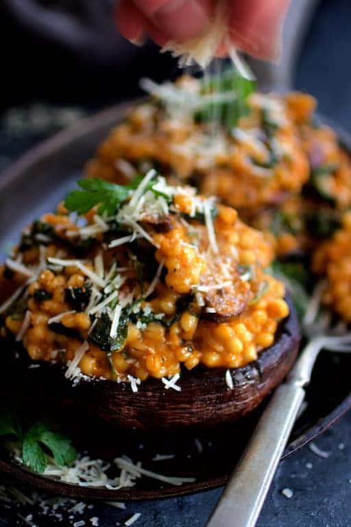 Photo of Barley Risotto Stuffed Portobello Mushrooms being sprinkled with Parmesan cheese.