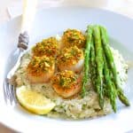 Pistachio Encrusted Scallops with Champagne Risotto and Roasted Asparagus on white plate with ornate fork.