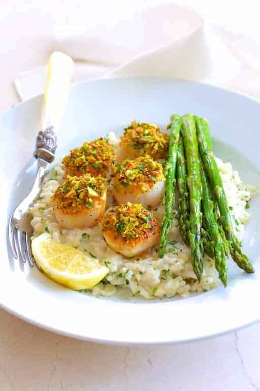 Pistachio Encrusted Scallops with Champagne Risotto and Roasted Asparagus on white plate with ornate fork.