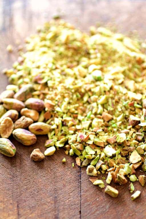 Photo of ground pistachios on wood surface with some left whole.