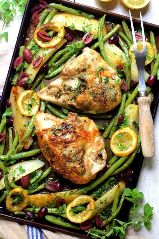 Photo of Sheet Pan Roast Chicken with Potatoes Green Beans Olives and Lemon garnished with fresh oregano.