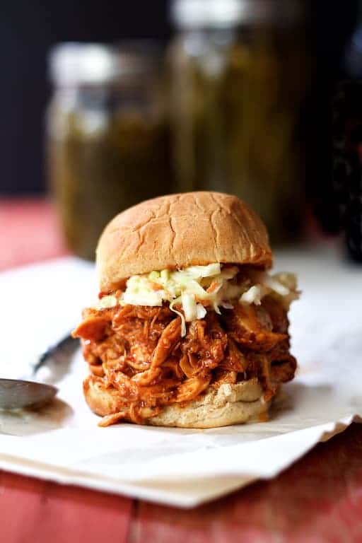 Sweet and Spicy Barbecue Chicken Slider on paper with pickles in the background.