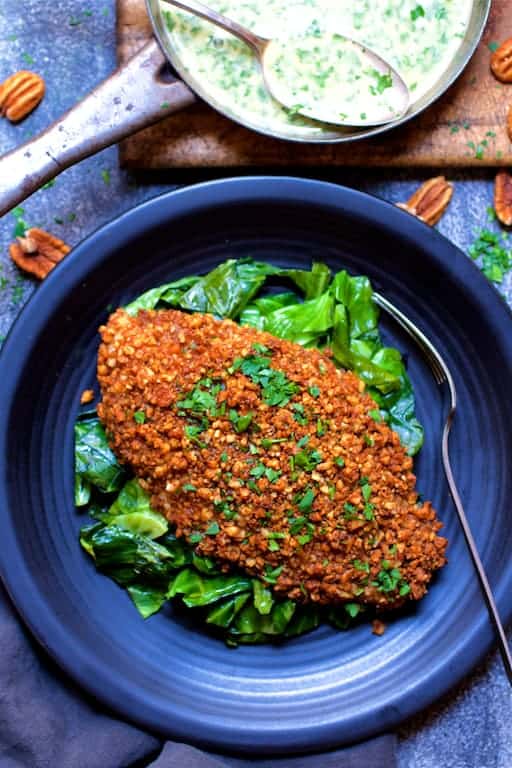 Photo of Baked Catfish Pecan Meuniere with Spicy Sauteed Greens on black plate.