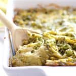 Baked Orzo with Pesto Peas Prosciutto and Mascarpone in white baking dish with wooden spoon scooping some out.