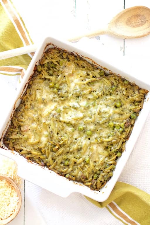 Photo of Baked Orzo with Pesto Peas Prosciutto and Mascarpone on white wooden background.