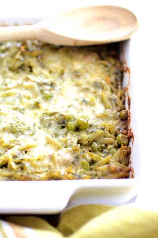 Photo of Baked Orzo with Pesto Peas Prosciutto and Mascarpone in white baking dish before being served.