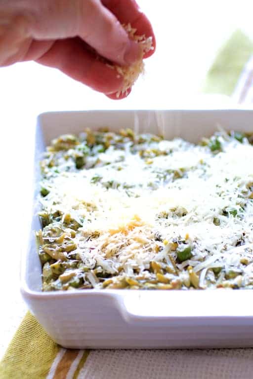 Photo of cheese being sprinkled over Baked Orzo with Pesto Peas Prosciutto and Mascarpone before being baked.