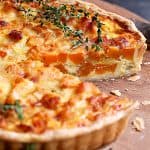 Butternut Squash Leek and Gruyere Tart on wood cutting board with piece removed.