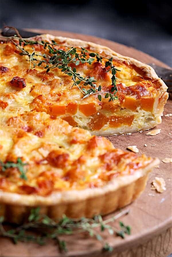 Butternut Squash Leek and Gruyere Tart on wood cutting board with piece removed.