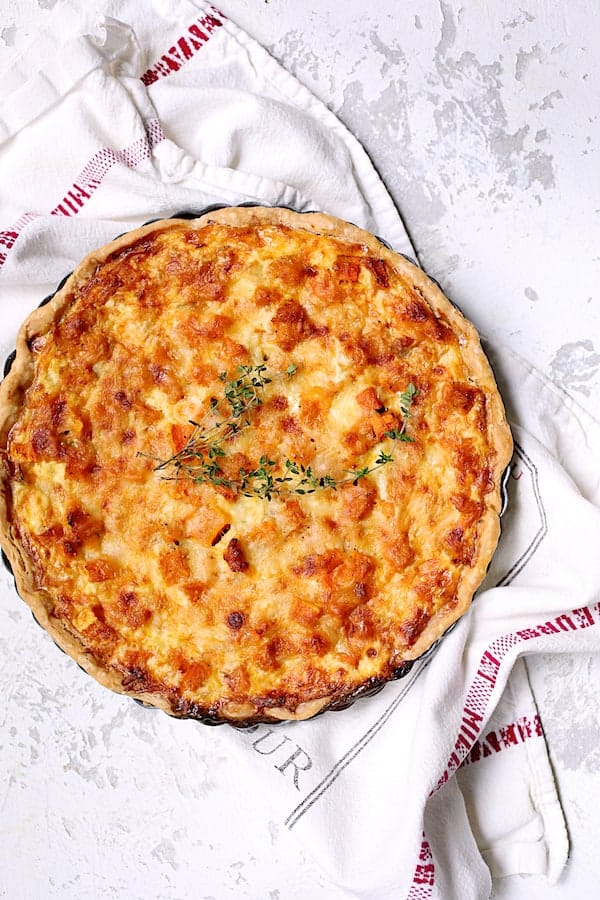 Photo of whole Butternut Squash Leek and Gruyere Tart on white printed towel garnished with fresh thyme.