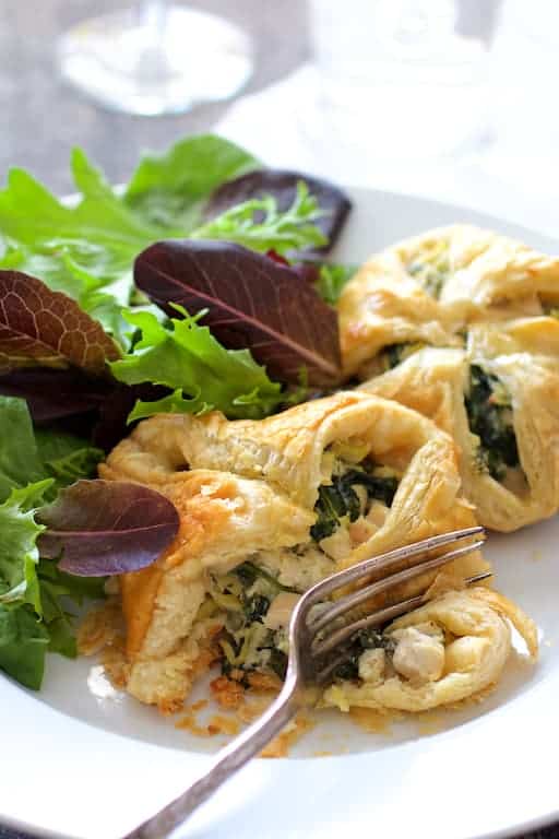 Photo of Chicken Spinach and Artichoke Puff Pastry Parcels on white plate cut into with a fork.