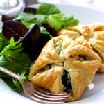 Two Chicken Spinach and Artichoke Puff Pastry Parcels on white plate with salad greens and fork.