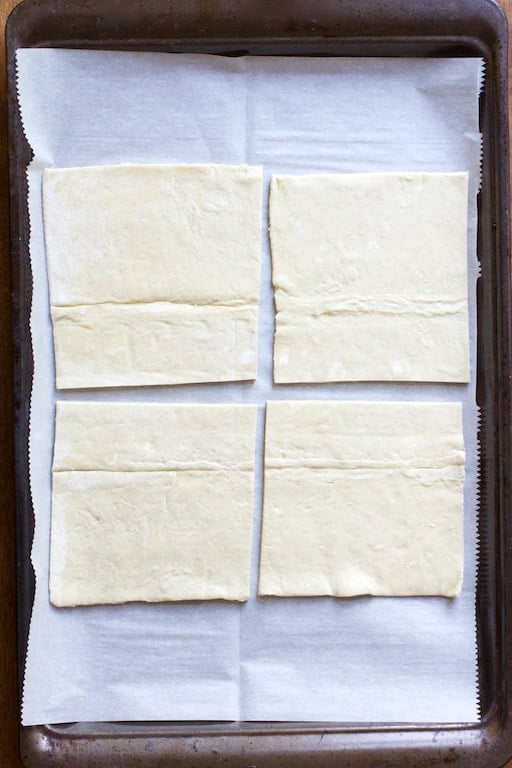 Process photo of four pieces of puff pastry on parchment paper-lined baking sheet.