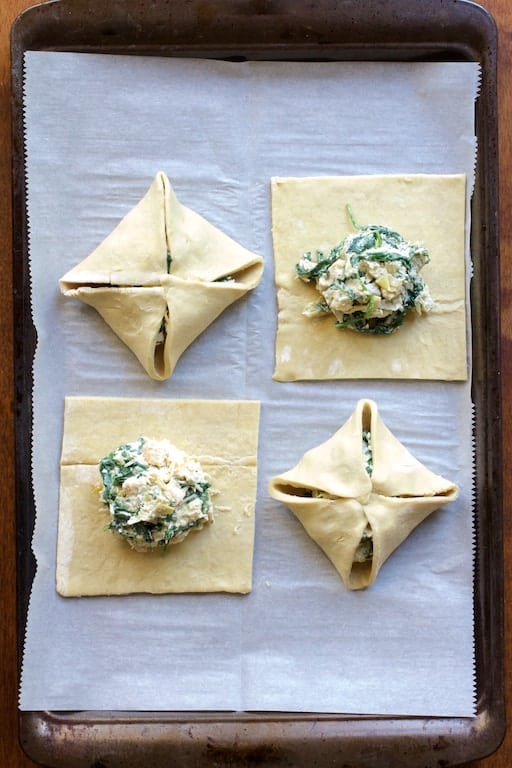Photo of four parcels on parchment paper-lined baking sheet with filling--two folded, two not yet folded before baking.