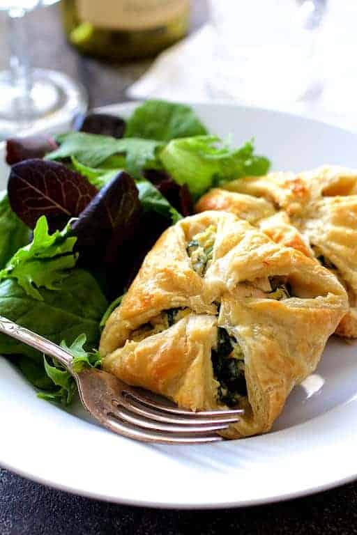 Two Chicken Spinach and Artichoke Puff Pastry Parcels on white plate with salad greens and fork.